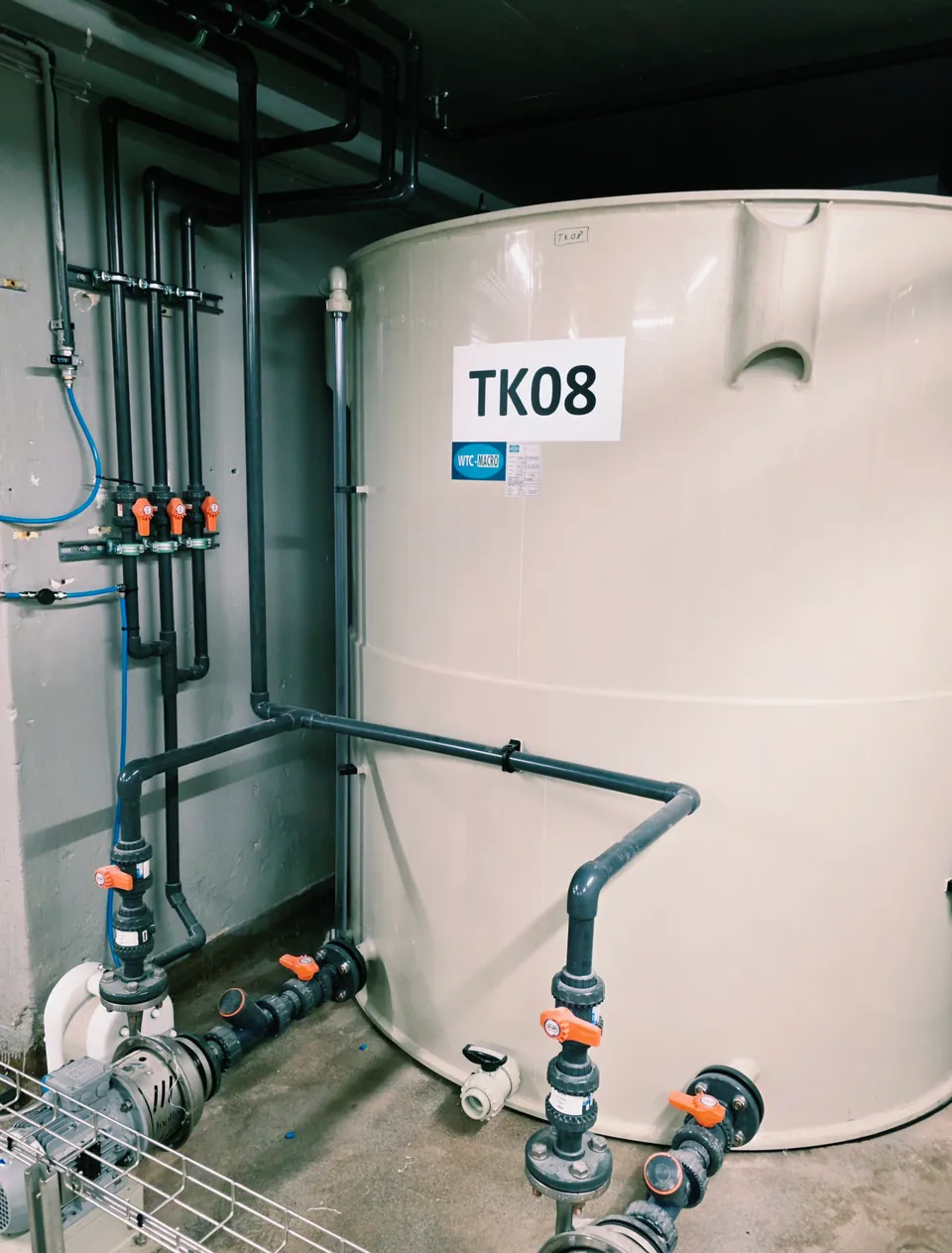 Ljus processtank med anslutna rör och orange ventilhandtag