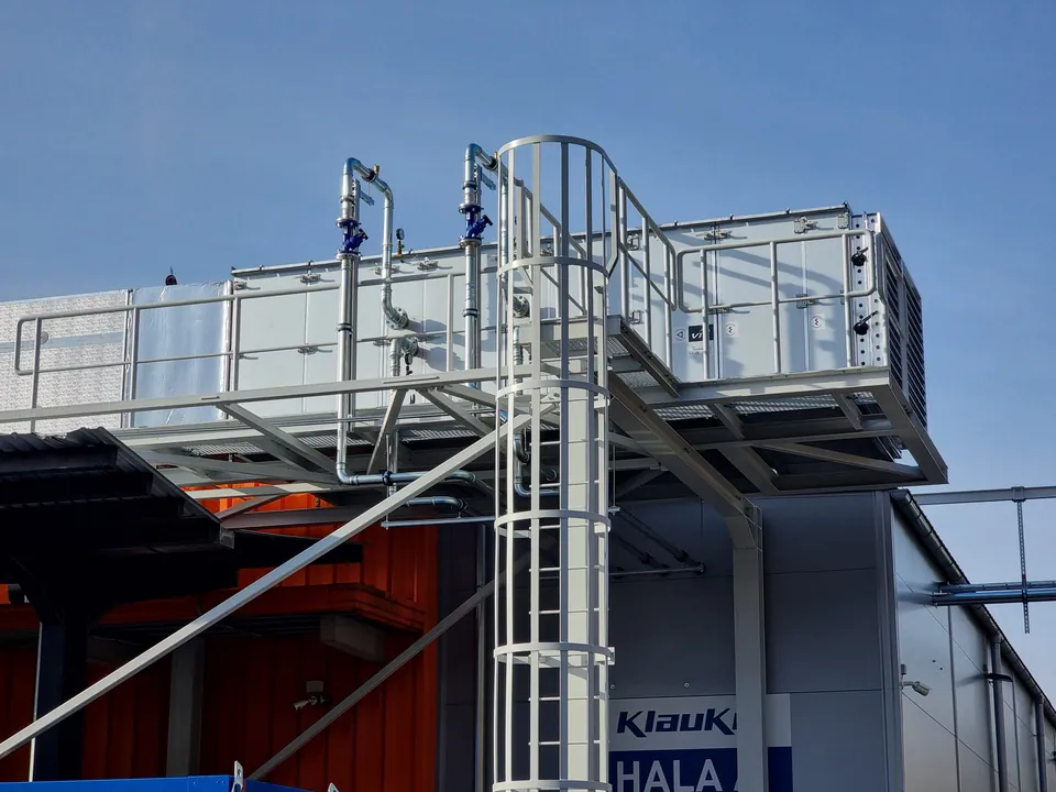 Ventilationsaggregat med röranslutningar och serviceplattform utanför en industribyggnad